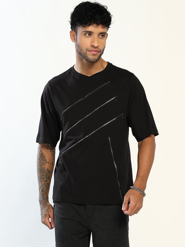 A man wearing a black short-sleeve t-shirt with diagonal glossy silver zipper-like graphic details on the front, paired with black pants, against a plain white studio background.