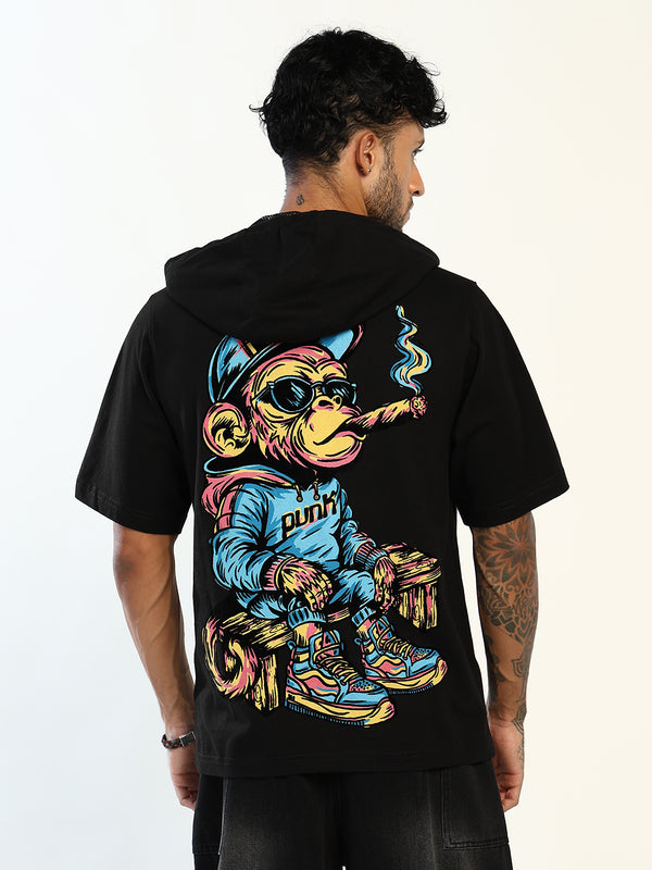 A man shown from the back wearing a black short-sleeve hoodie with a large colorful graphic of a cartoon monkey in a blue tracksuit smoking a cigar. The word 'PUNK' is printed on the tracksuit.