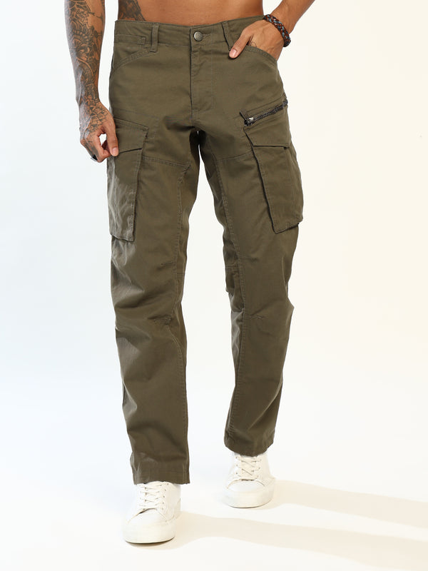 A person modeling olive green cargo pants with zippered and flap pockets, paired with white sneakers against a plain white studio background.