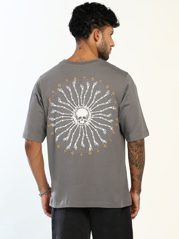 A man wearing a gray t-shirt, viewed from the back. The shirt features a large graphic print of a skull surrounded by a circular pattern of white arrows and small gold stars on a light gray background.